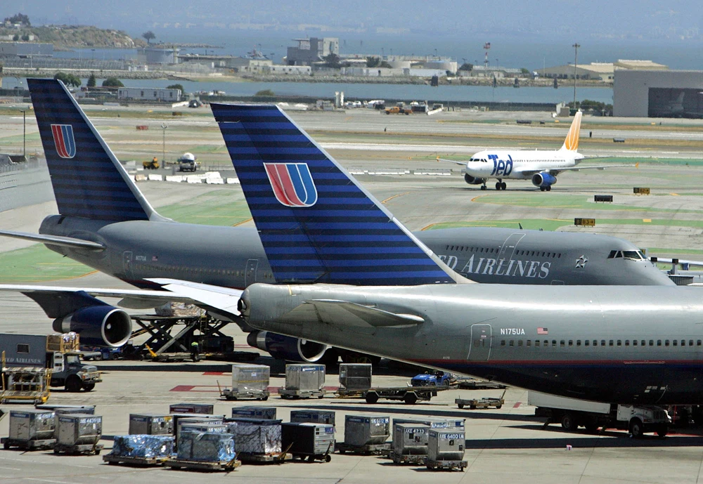 Multiple United Airlines aircraft parked at an airport gate, with visible loading operations and cargo containers.