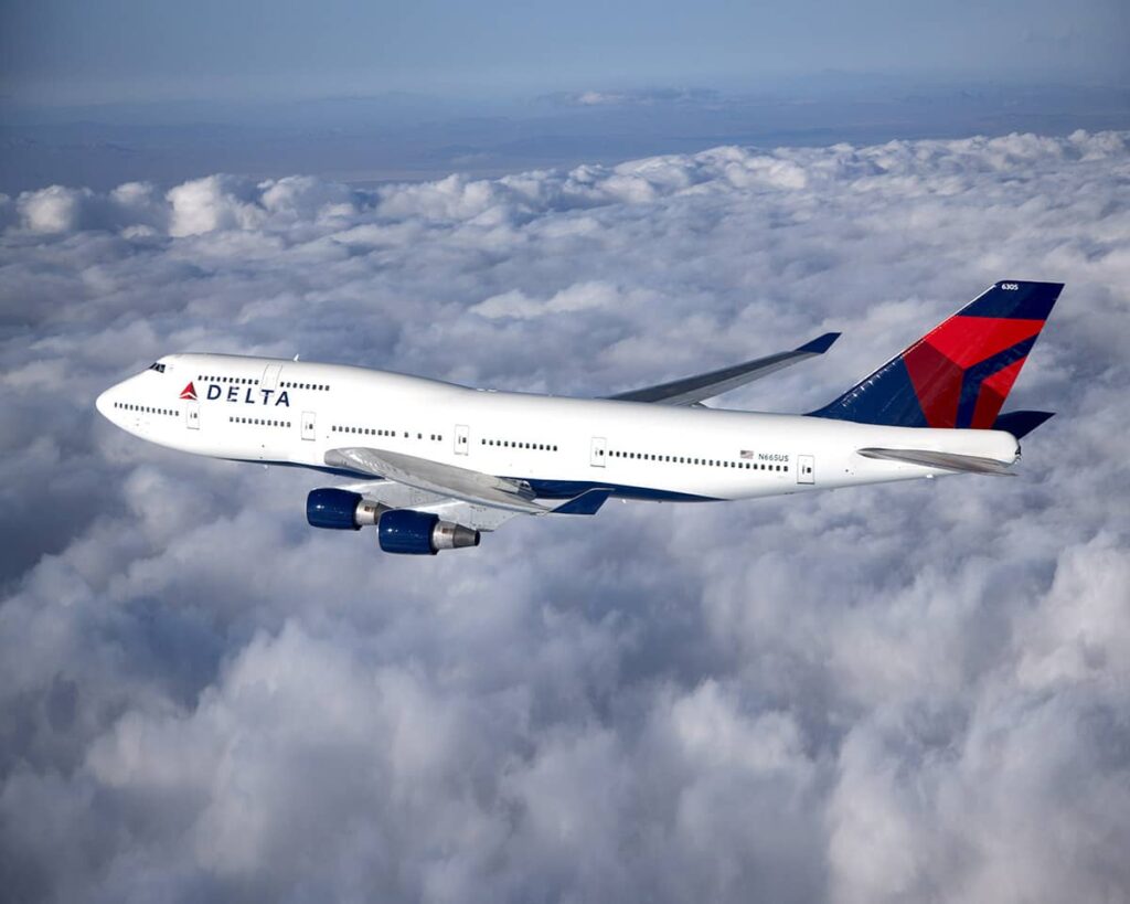 Delta Air Lines Boeing 747 aircraft flying above the clouds, with the airline’s red and blue logo visible on the tail.
