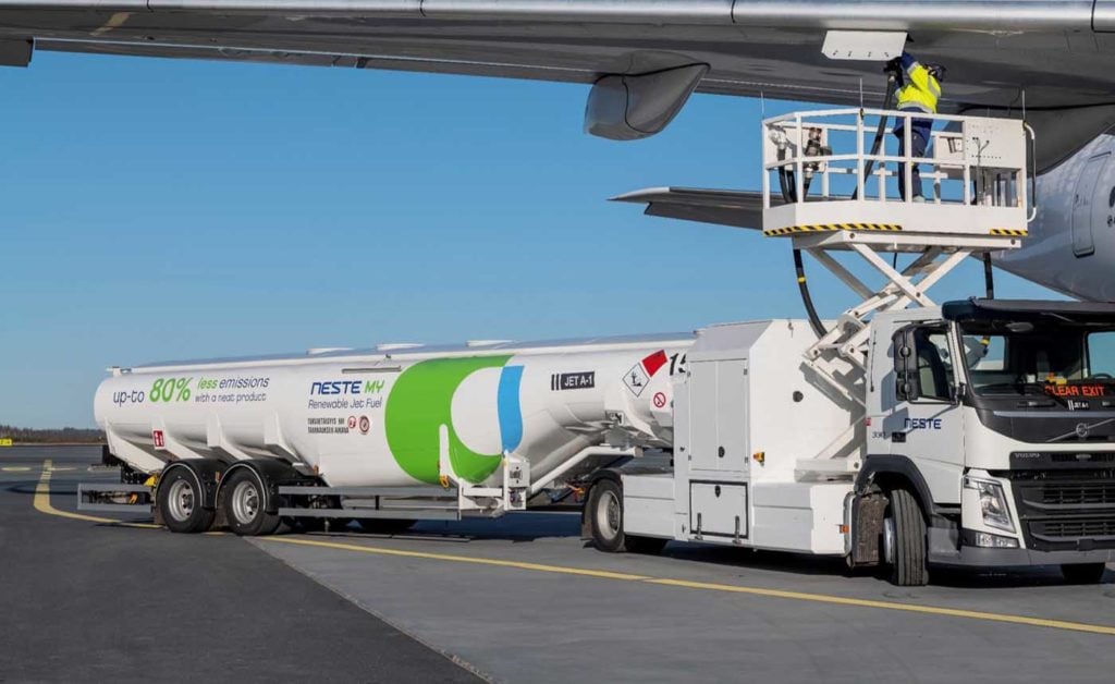 A fuel truck labeled ‘Sustainable Aviation Fuel’ parked near an aircraft on an airport tarmac, representing efforts to reduce aviation’s environmental impact through alternative fuel sources.