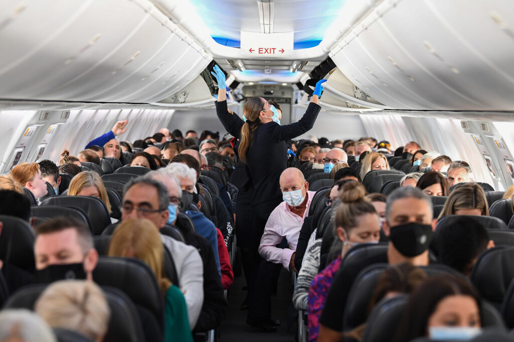 Airline passengers seated in an aircraft cabin wearing face masks during the COVID-19 pandemic, highlighting health and safety measures in air travel.