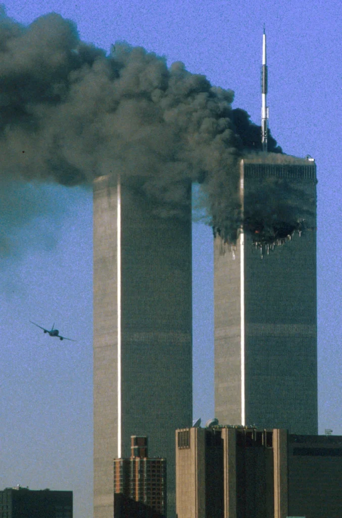 A commercial airplane approaching the South Tower of the World Trade Center in New York City, moments before impact during the September 11, 2001 terrorist attacks. The North Tower is already emitting thick black smoke from a previous impact.